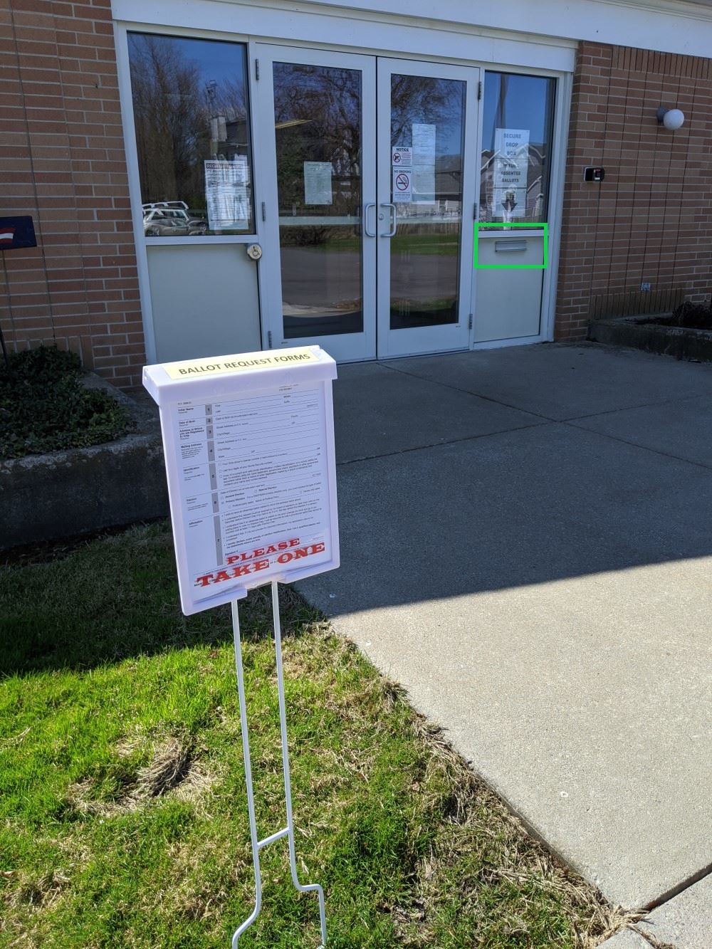 a picture of the front door of the board of elections office with a box of ballot request forms in t